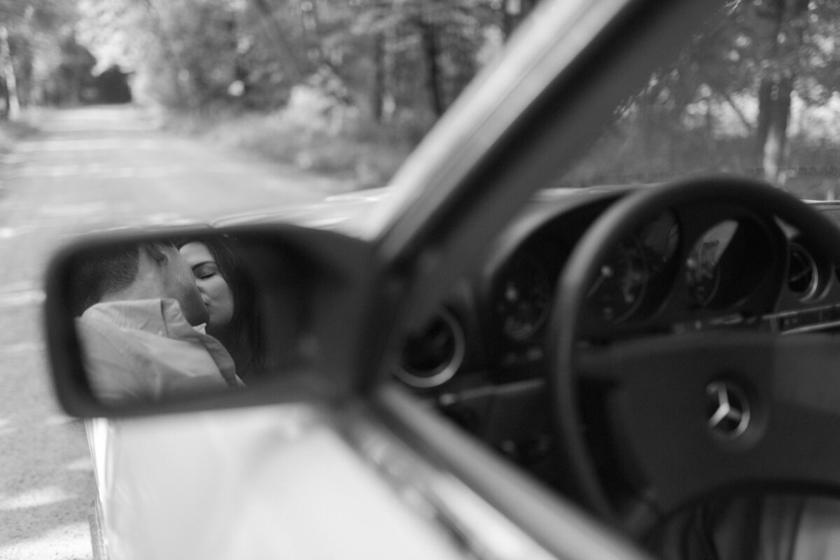 Couple kissing in the rear view mirror of a classic car.
