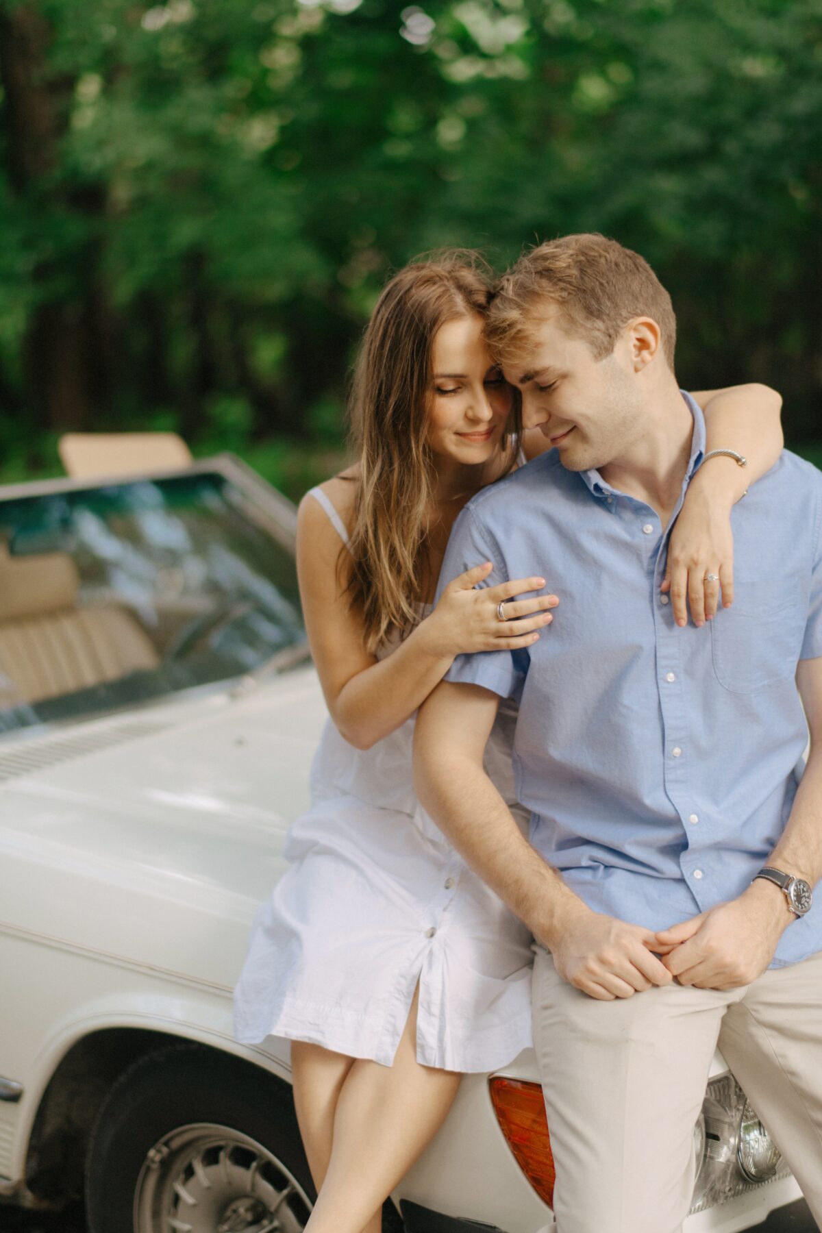 A couple posing on the hood of a classic car.